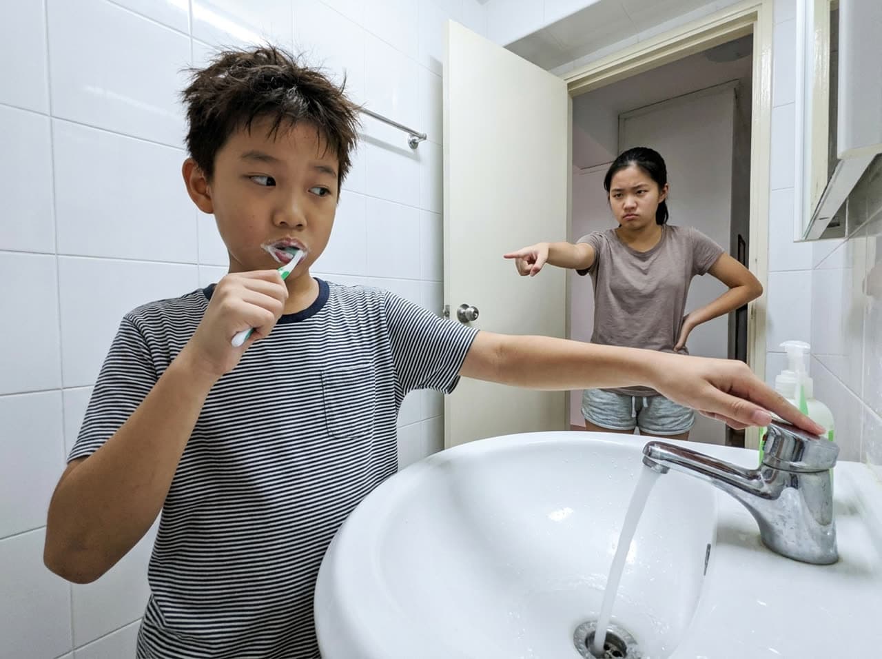 男孩刷牙时开着水龙头，姐姐提醒他把水关掉。