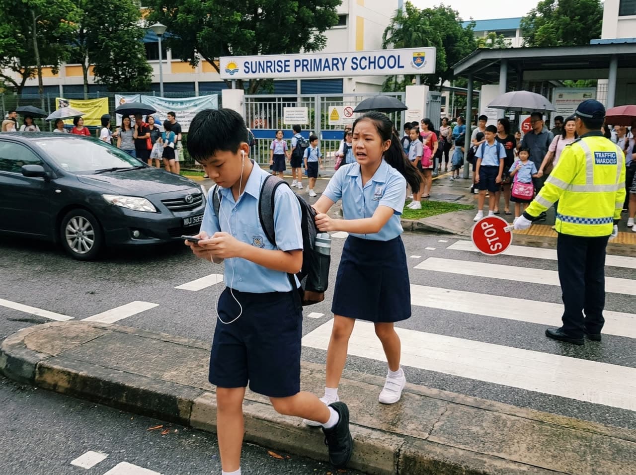 男孩戴着耳机看手机过马路,身后的同学急忙拉住他的书包。